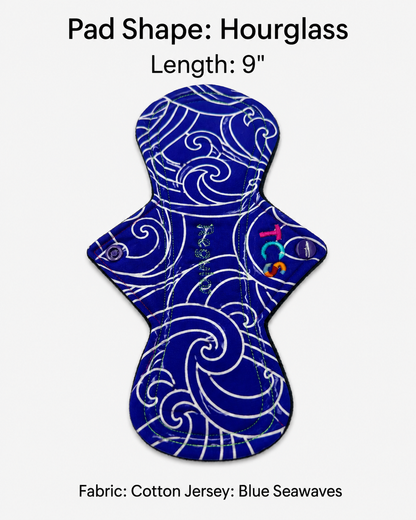 An hourglass-shaped cotton jersey menstrual pad with a white swirling wave pattern on a deep blue background, shown on a light gray background with text reading 'Pad Shape: Hourglass', 'Length: 9"', and 'Fabric: Cotton Jersey: Blue Seawaves'.