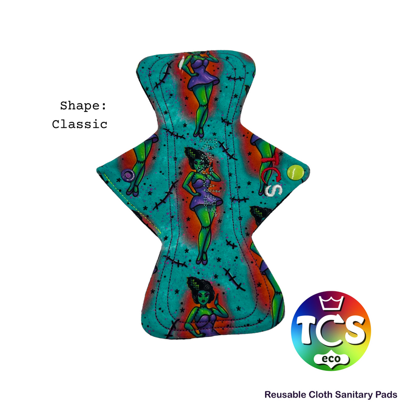 A Classic shaped Reusable Cloth Sanitary Pad by TCS-eco.  The pad has frankenzombie cotton jersey top fabric.  The image also have a TCS-eco logo and reusable Cloth Sanitary Pads on the bottom right corner.
